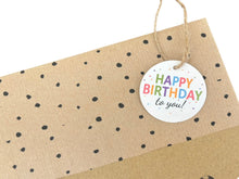 Load image into Gallery viewer, A close-up of a kraft paper gift bag with black confetti dots and a round white hanging tag that reads “HAPPY BIRTHDAY to you!” in colorful lettering, tied with twine on a white background.
