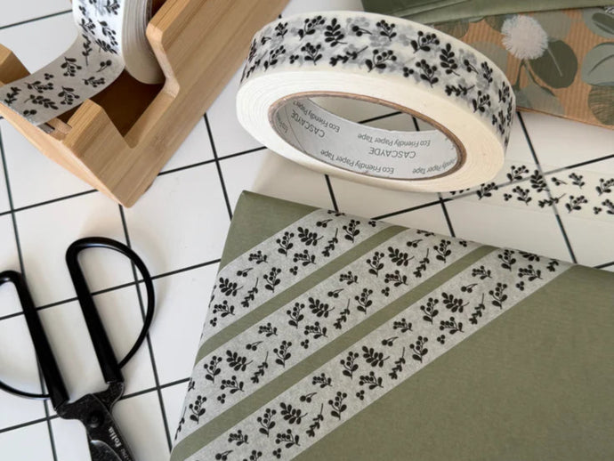 Decorative tape with floral pattern on a white surface with scissors and a wooden holder.