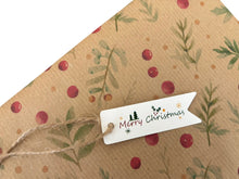 Load image into Gallery viewer, A close-up of a kraft paper envelope or gift bag with a watercolor-style holiday print of green leaves and red berries, tied with twine and a small white paper tag that reads “Merry Christmas.”.
